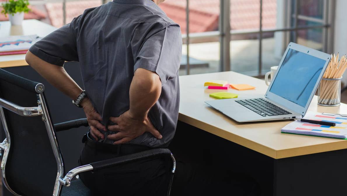 Une personne assise à un bureau se tient le bas du dos